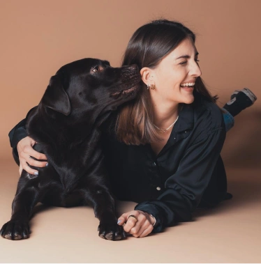 Frau kuschelt lachend mit ihrem schwarzen Hund